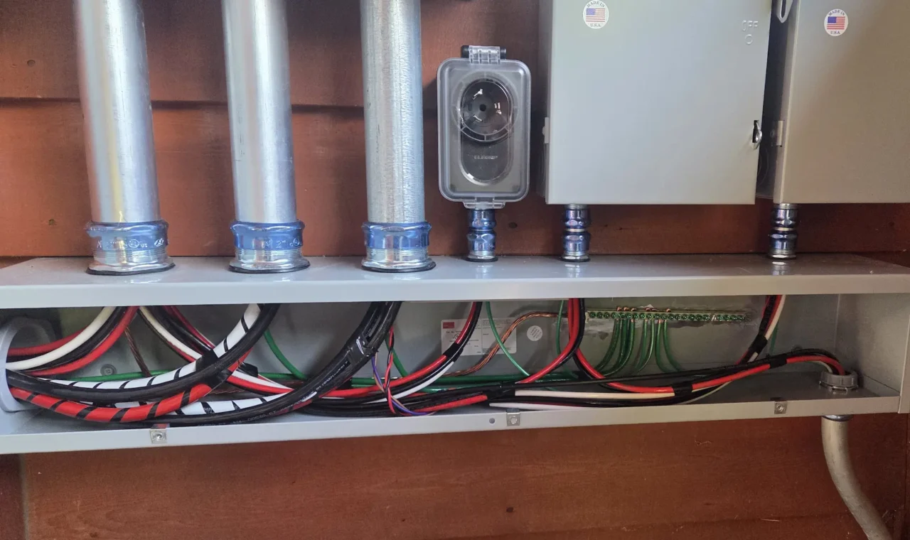 Open electrical panel with bundled colored wiring, metal conduits, and control boxes.