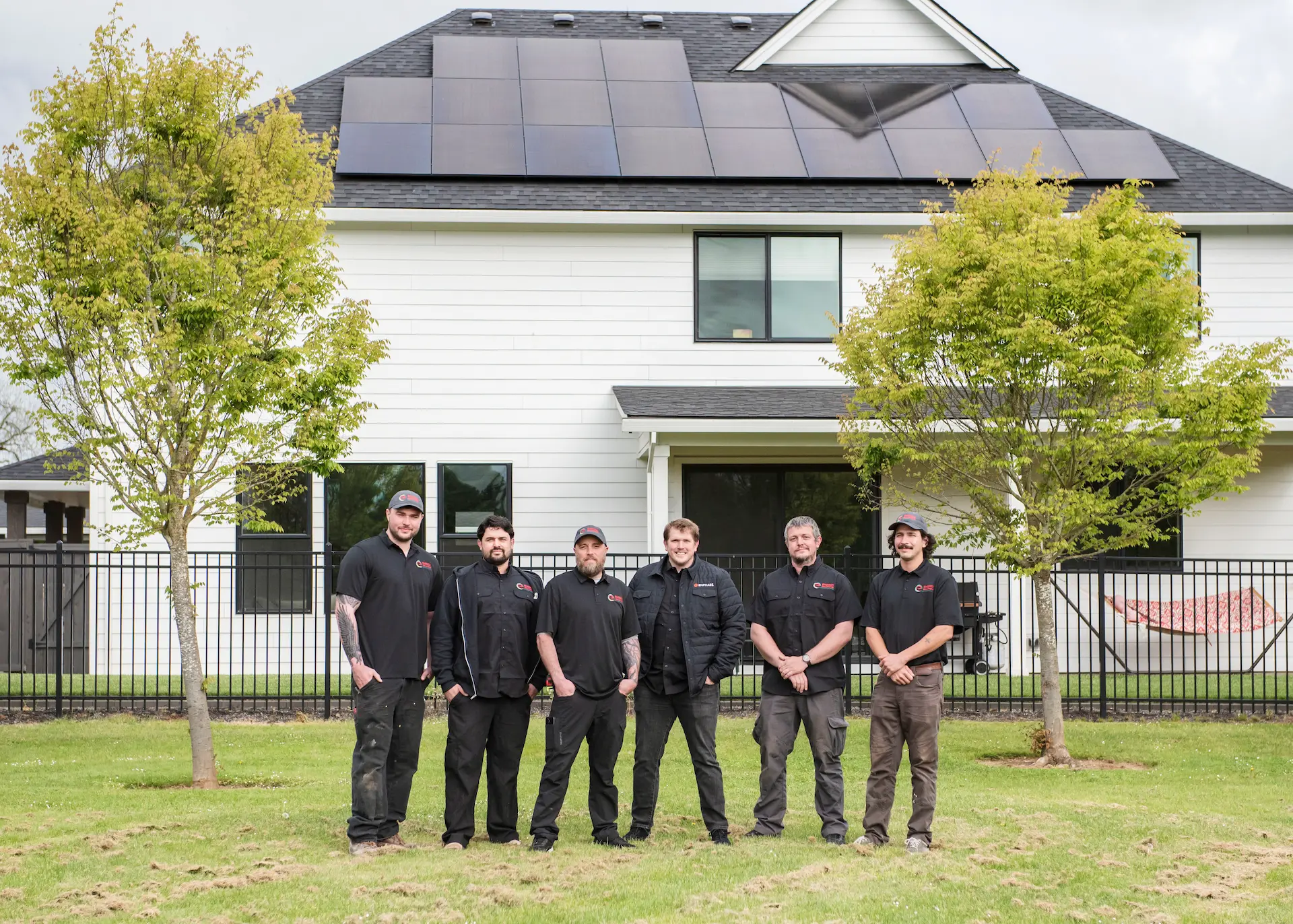 Solar team in black poses before white house, cloudy day.