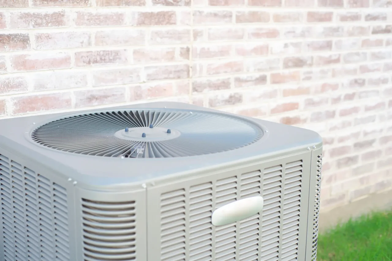 Outdoor AC condenser unit beside brick wall.