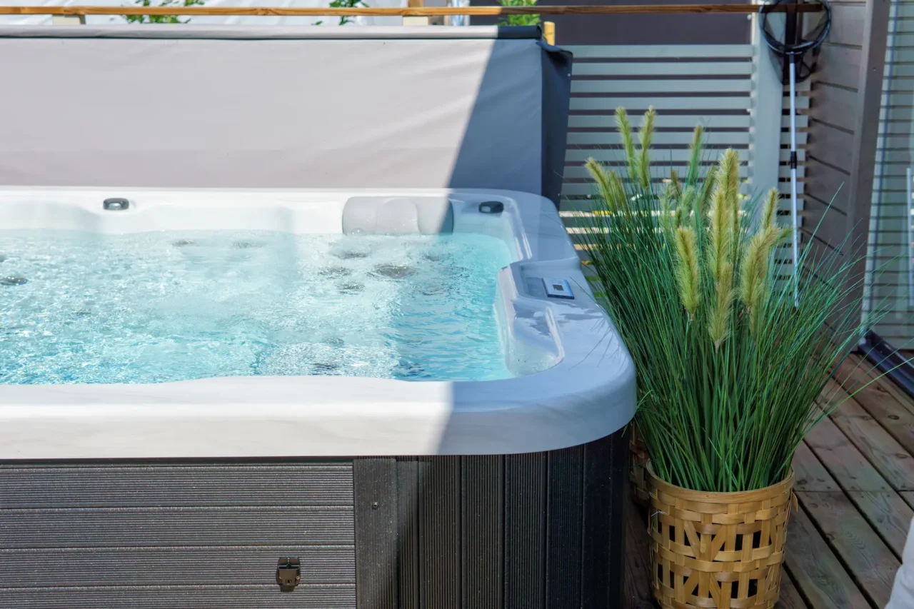 Bubbling hot tub on sunny deck beside potted grass.