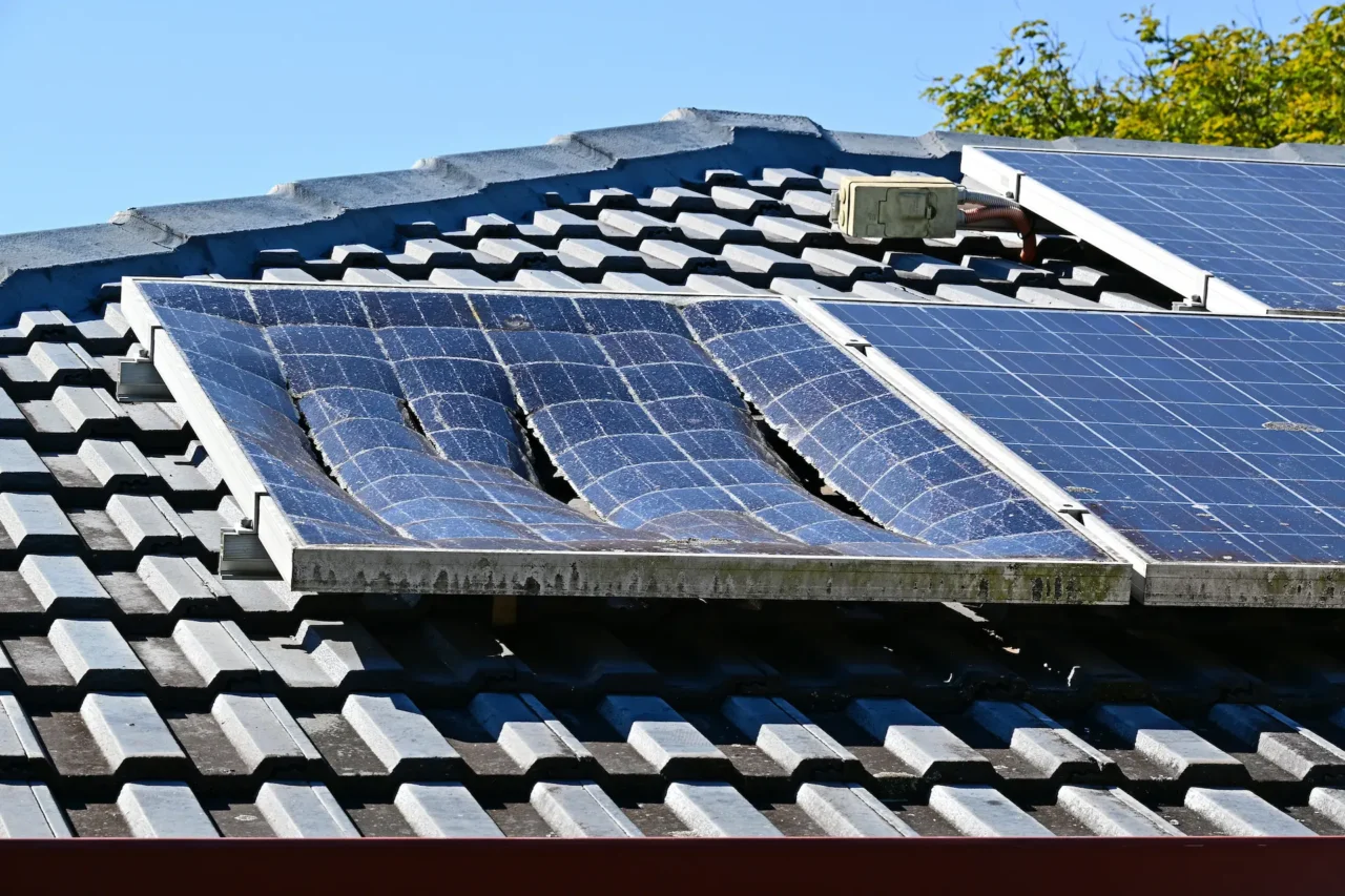 Warped solar panels on dark tiled roof under blue sky.