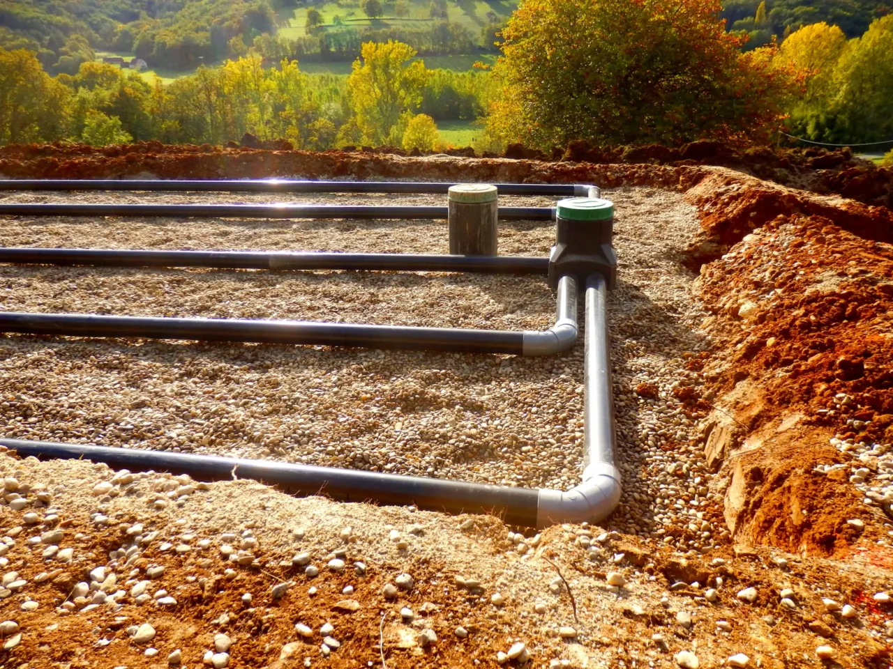 Septic system pipes in gravel bed with rural backdrop.