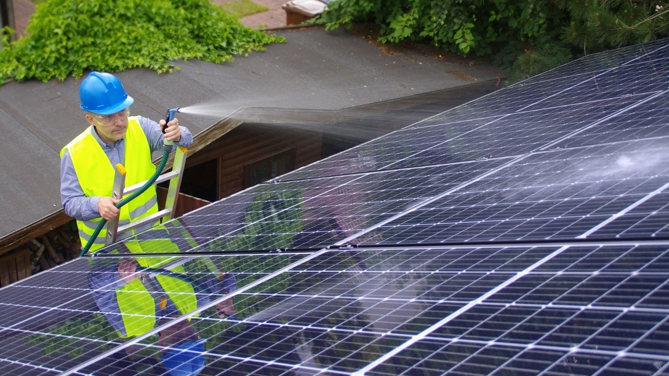 man spraying solar panels with hose to clean them