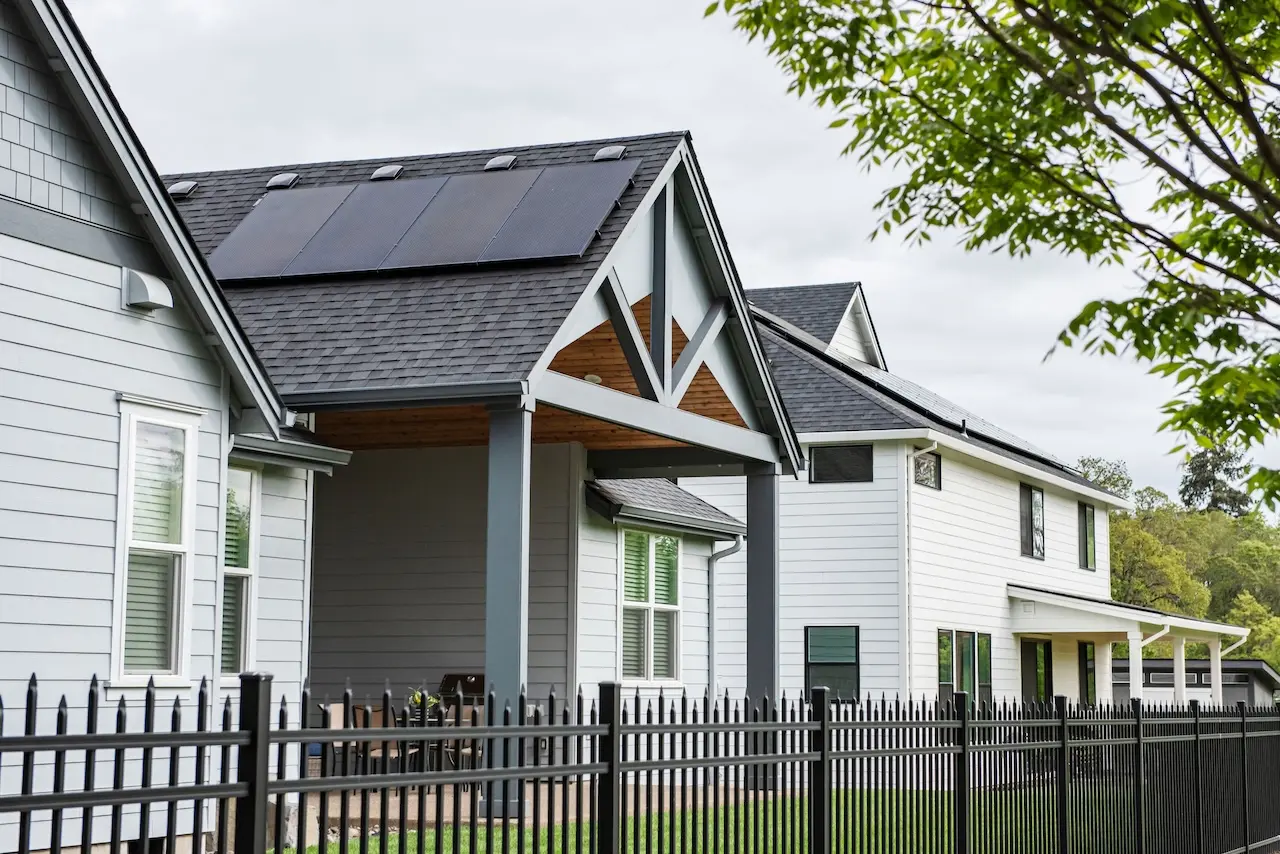 Modern home with rooftop solar panels behind iron fence.