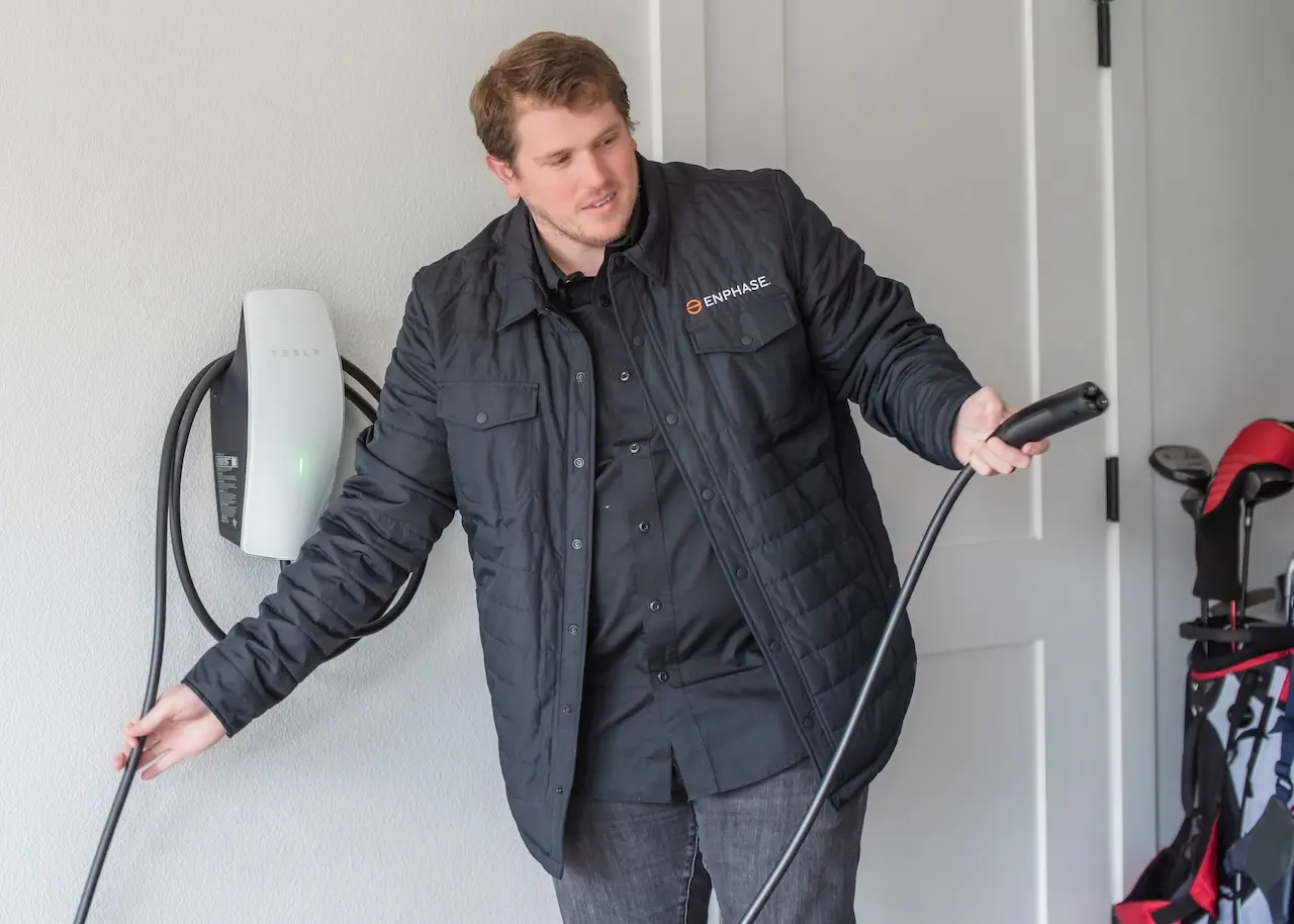 Man in Enphase jacket holds Tesla EV charger in garage.